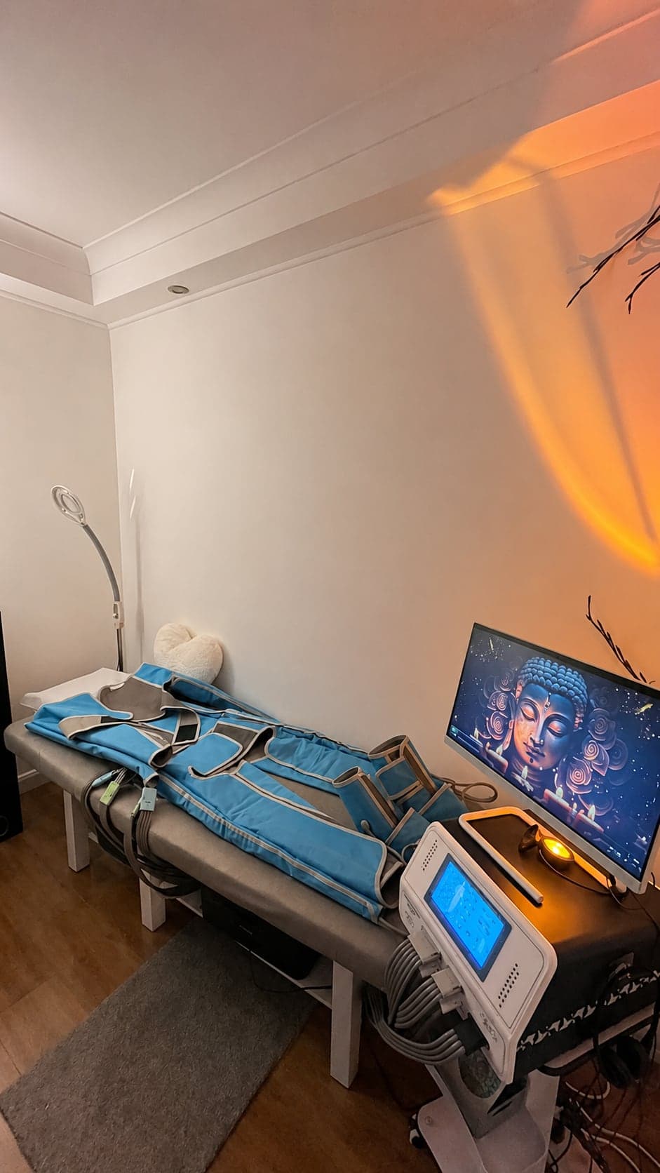 The Sunsmile pressotherapy room — the compression suit laid out on the treatment bed beside the machine, warm lamp light on the wall