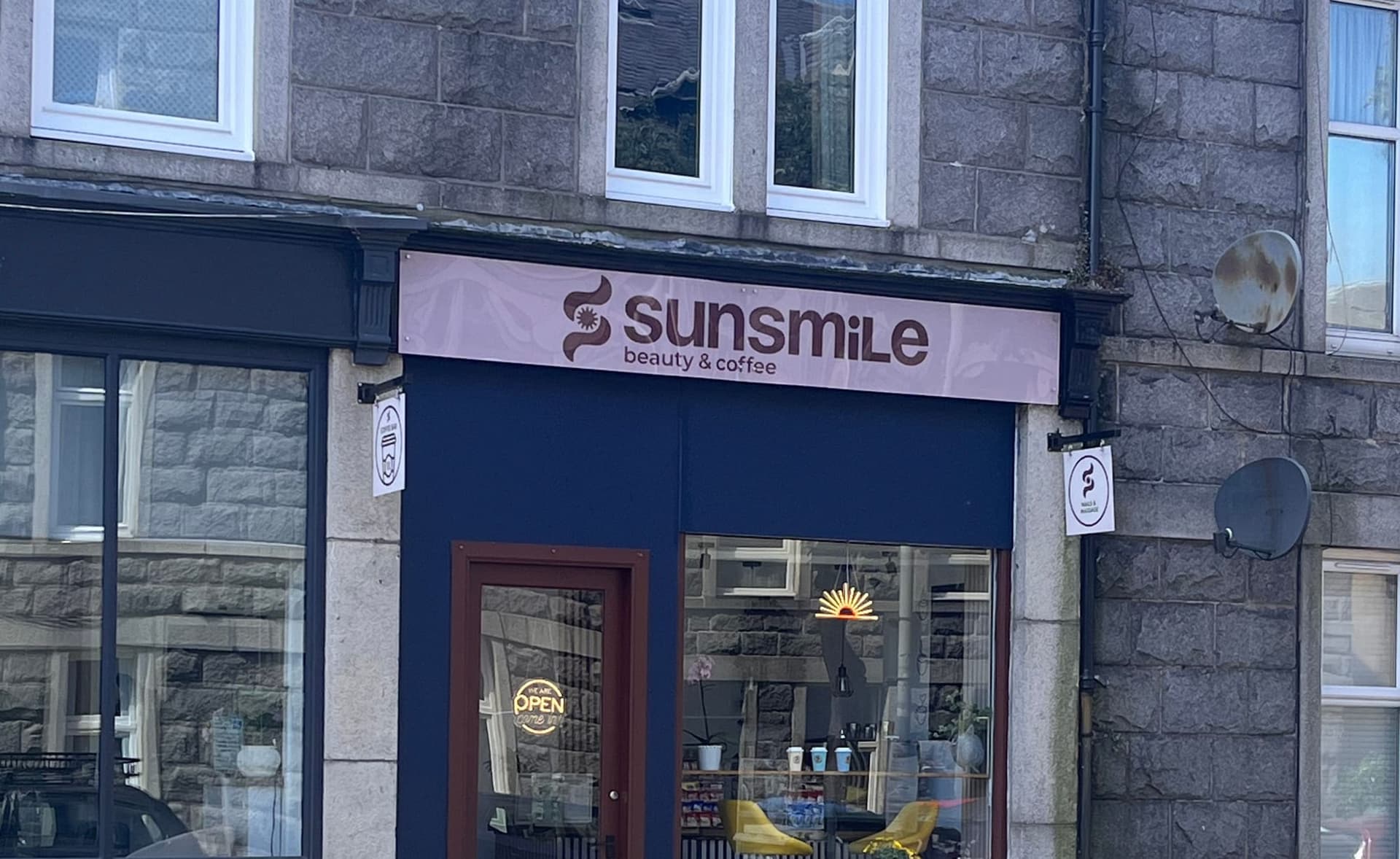 The Sunsmile shopfront on Great Western Place — pink sign reading Sunsmile beauty & coffee above a deep navy frontage, burgundy door and a neon sun in the window