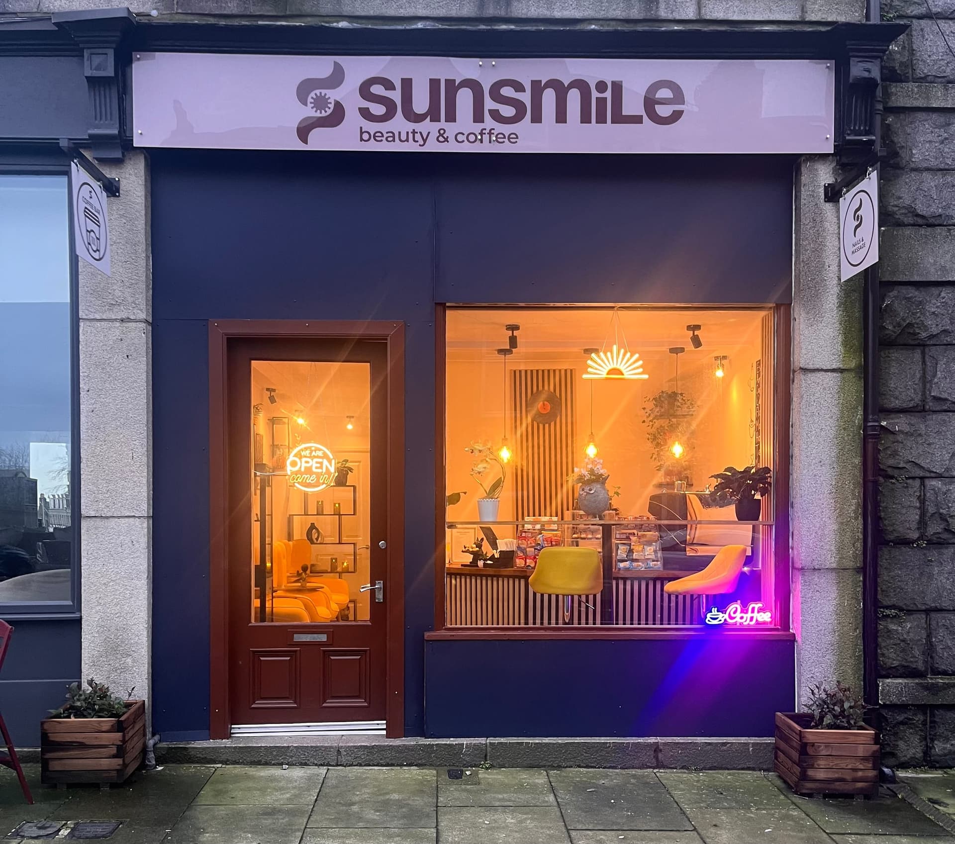 Sunsmile storefront at dusk — deep navy facade with a neon sun and 'open, come in' glow